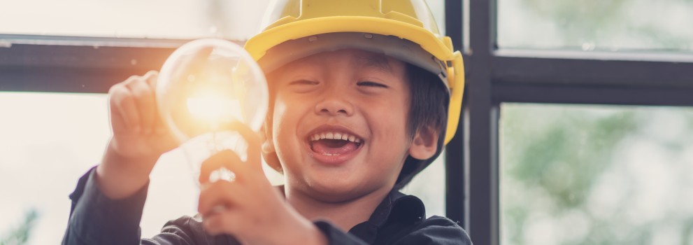 A child wearing a safety helmet holds a light bulb.