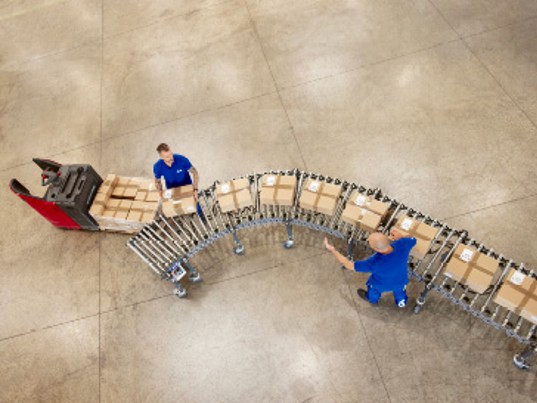 Collaborateurs GLS manipulant des colis sur une ligne de tri dans un entrepôt logistique, illustrant les procédures opérationnelles et la conformité des processus au sein du groupe.