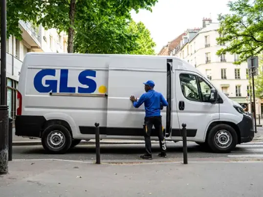 Livreur GLS à côté d'une camionnette de livraison blanche GLS stationnée en ville.
