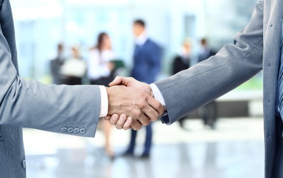 Hands reaching out for a business handshake in front of a professional setting.